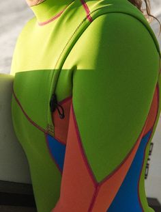 a woman in a green and orange wetsuit holding a surfboard