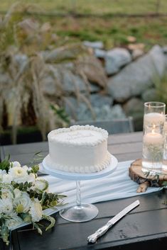 a white cake sitting on top of a table next to flowers and two candles in front of it