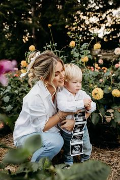 a woman holding a child in front of flowers