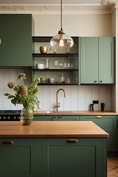 a kitchen with green cabinets and wooden counter tops, an island in front of the sink