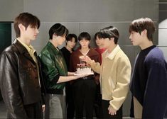 a group of young men standing next to each other holding a cake with candles on it