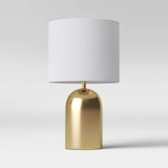 a gold table lamp with a white shade on the base and a light in the middle