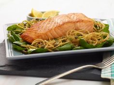 salmon with noodles and spinach on a plate next to lemon wedges in a bowl