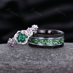 two wedding rings with green and purple stones on top of each other, sitting on a rock