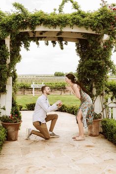 a man kneeling down next to a woman in front of a gazebo with greenery on it