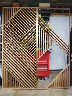 a garage with a large wooden structure on the wall and red cart in front of it