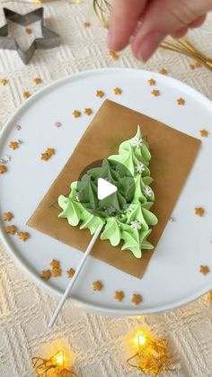 someone is decorating a cake with green icing and sprinkles on a white plate