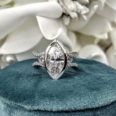 a diamond ring sitting on top of a blue velvet cushion next to flowers and white petals