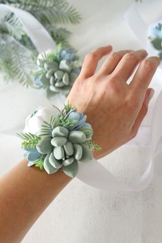 a woman's hand holding onto a white ribbon with succulents on it