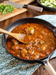 a skillet filled with meat and vegetables on top of a wooden table next to a cutting board