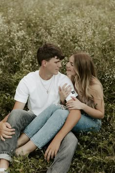 a young man and woman sitting in the grass with their heads close to each other