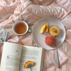 an open book and two peaches on a bed next to a cup of tea