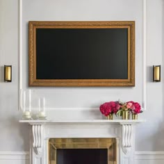 a fireplace in a living room with a painting on the wall above it and vases filled with flowers