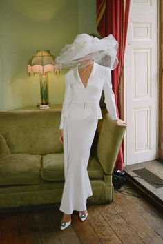 a woman in a white dress and veil standing next to a couch