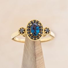 an oval blue stone surrounded by black and white diamonds sits on top of a wooden stand