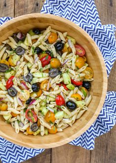 a wooden bowl filled with pasta salad on top of a blue and white napkin