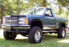 a large green truck parked on top of a lush green field