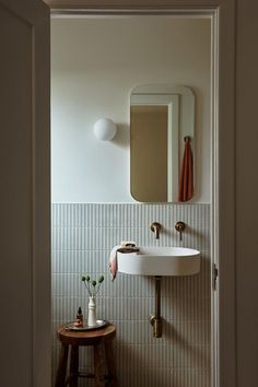 a white sink sitting under a bathroom mirror next to a table with flowers on it