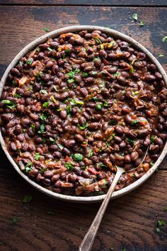 a large bowl filled with beans and parsley on top of a wooden table next to a spoon