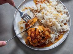 someone is holding a fork over a plate of food with rice and meat on it