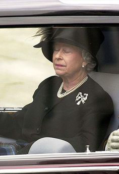 the queen is sitting in her car wearing a black hat and pearls on her necklace