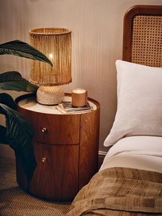 a nightstand with a candle and a plant on it next to a bed in a room