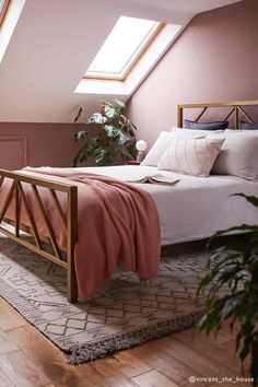 an attic bedroom with pink walls and white bedding, wooden frame headboard, potted plant, and skylight