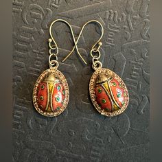 a pair of red and gold earrings on top of a black surface with writing in the background