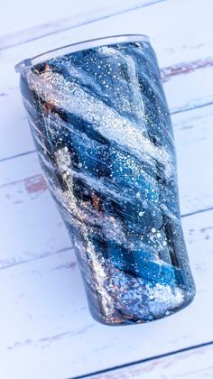 a blue and white tumbler sitting on top of a wooden table with snow flakes all over it