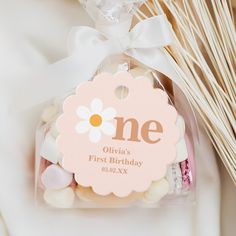 a pink and white birthday gift bag with marshmallows in it next to some sticks