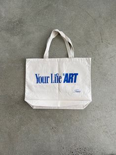 a white bag with the words your life art printed on it sitting on a concrete floor