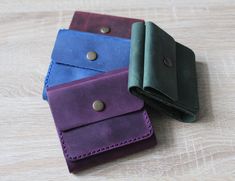 three different colored leather wallets sitting on top of a wooden table next to each other