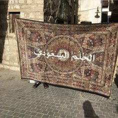 a large rug with arabic writing on it in front of a brick wall and sidewalk