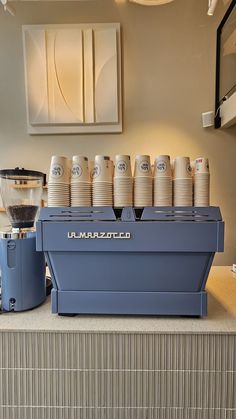 there is a coffee maker and cups on the counter in front of it that are lined up