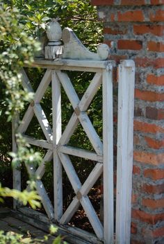 an old wooden gate with a bird statue on it's top, in front of a brick wall