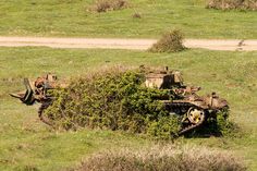 an old rusted out tank sitting in the middle of a grassy field next to a dirt road