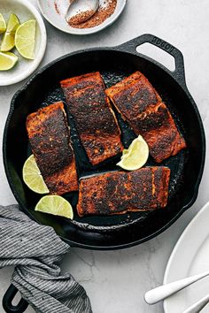 some fish are cooking in a skillet with lemons and spices on the side