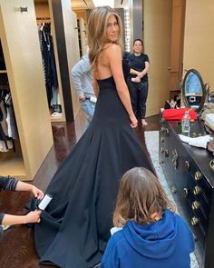 a woman in a black dress looking at herself in the mirror while another person looks on