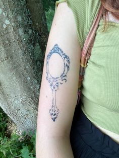 a woman with a tattoo on her arm is sitting next to a tree and looking at the camera