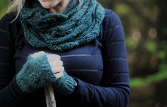 a woman wearing a green knitted scarf and holding a cane in her hands with trees in the background