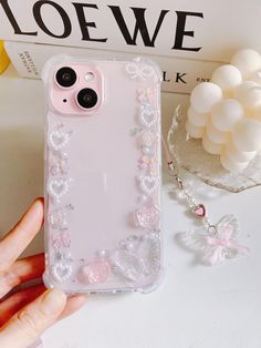 a person holding up a phone case with flowers and pearls on the back in front of a book