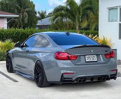 a grey bmw car parked in front of a house with palm trees and bushes behind it