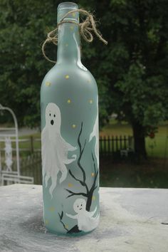 a painted glass bottle with ghost on it sitting on a table in front of some trees