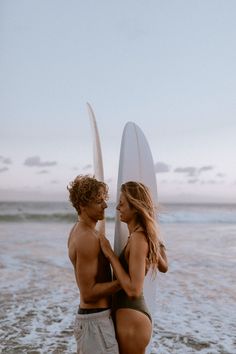 two people standing on the beach with surfboards