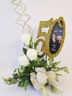 a bouquet of white roses and greenery in front of a 50th birthday photo frame