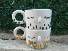 two coffee mugs sitting on top of each other with eyelashes painted on the cups