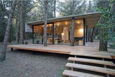 a wooden deck in front of a small cabin surrounded by trees with stairs leading up to it