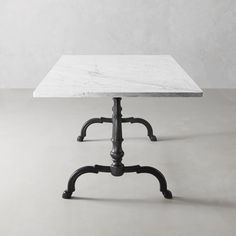 a white marble table with black legs and an iron base on a grey surface, in front of a gray wall