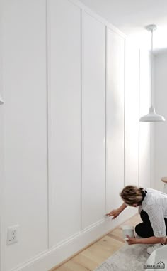 a woman is painting the wall in her living room with white walls and wood floors