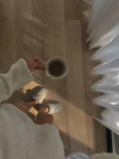 a person holding a cup of coffee on top of a wooden floor next to a window